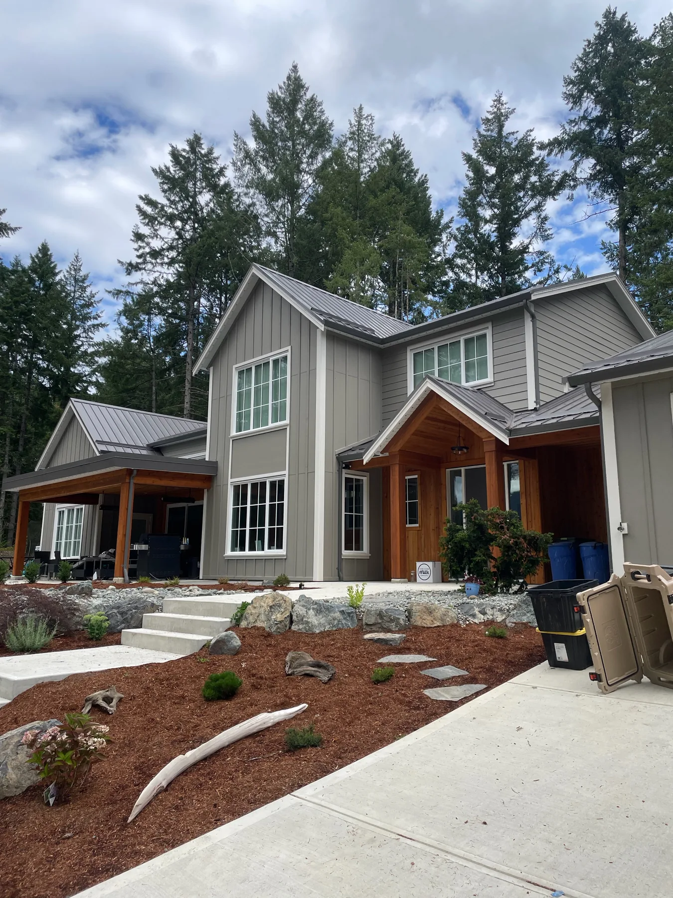 Gray painted two-story home with wood entry details and mature trees